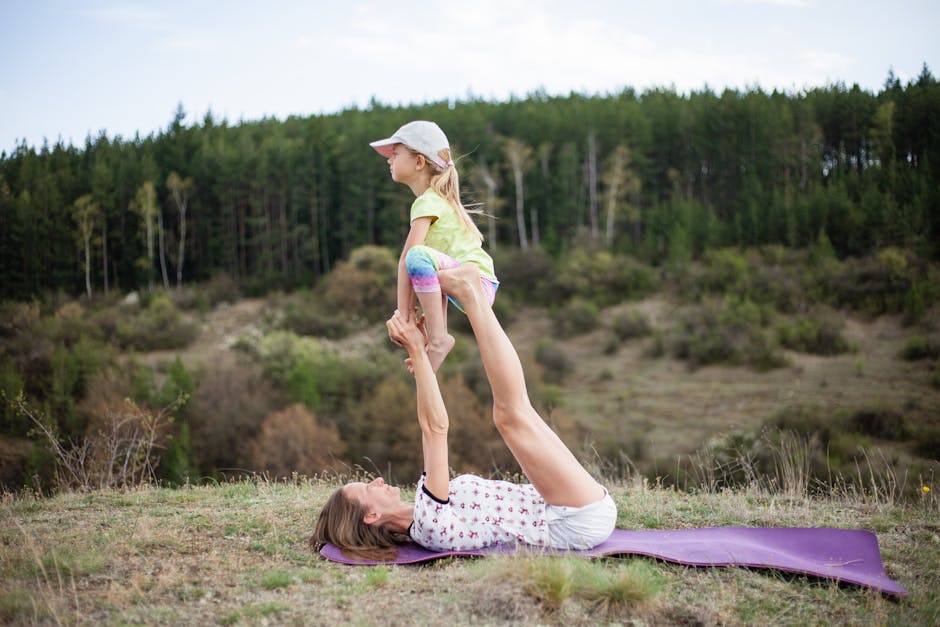A child and an adult doing a partner yoga pose together in a park on the grass.